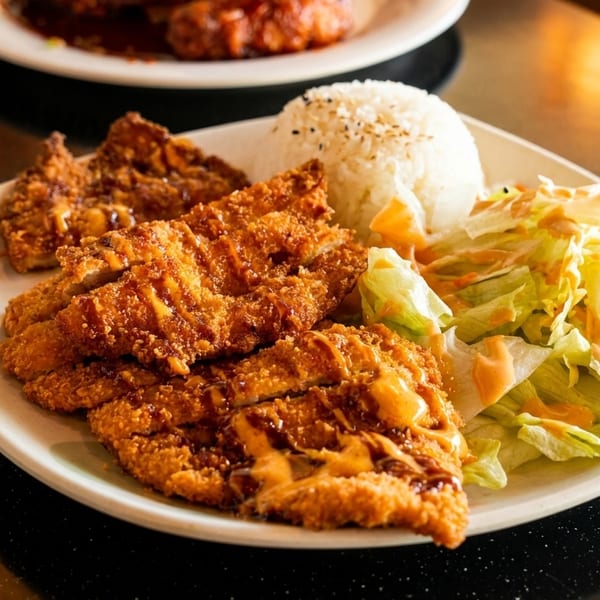 Crispy fried chicken cutlets with rice and a side salad on a white plate.