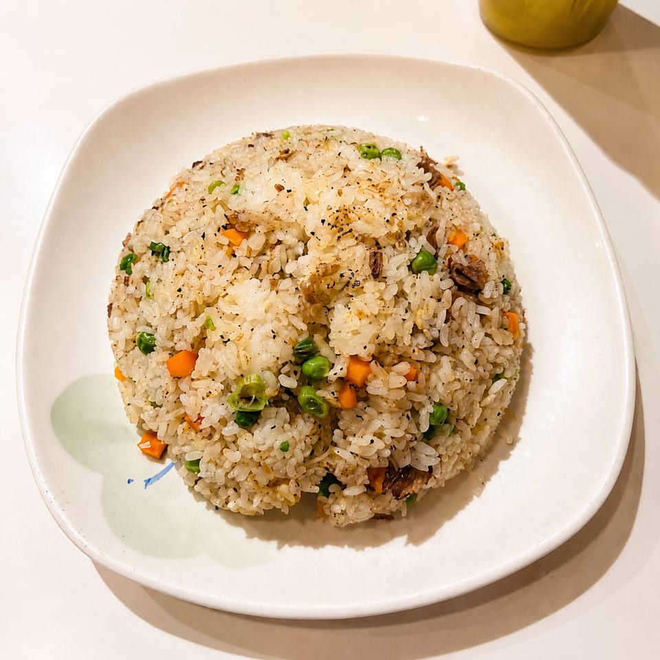 Mound of fried rice with peas, carrots, green onions, and mushrooms on a white plate.
