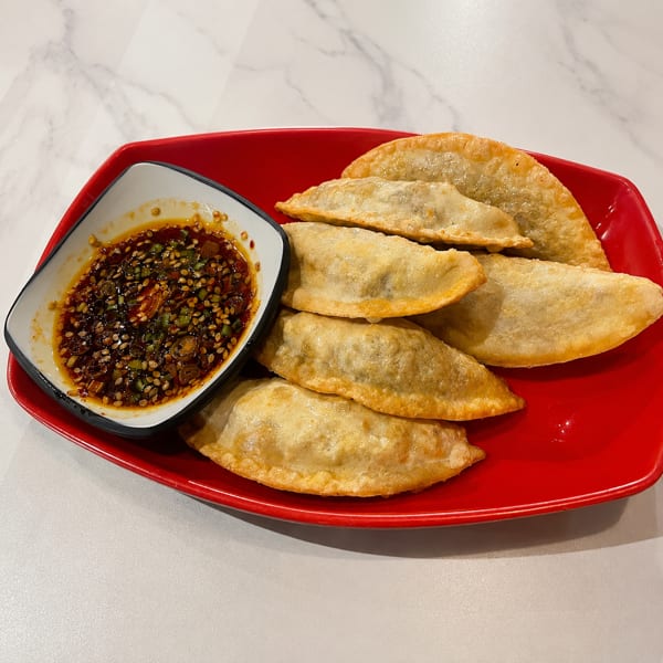 Golden-brown fried dumplings on a red plate with a side of chili oil dipping sauce.