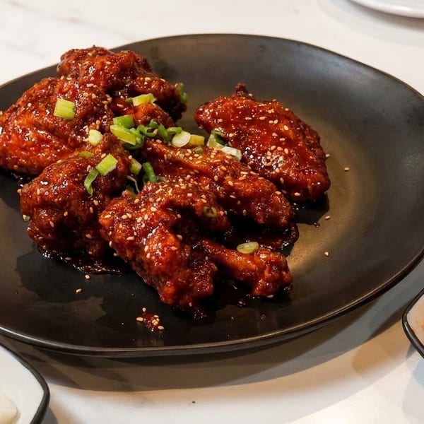 Sweet and spicy Korean fried chicken wings with sesame seeds and green onions, served with kimchi.